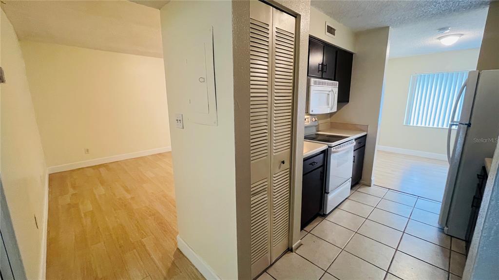 A kitchen with tile flooring, dark cabinets, and a white stove, adjacent to a living area — 7504 NEEDLE LEAF PLACE UNIT 68, TAMPA, FL
