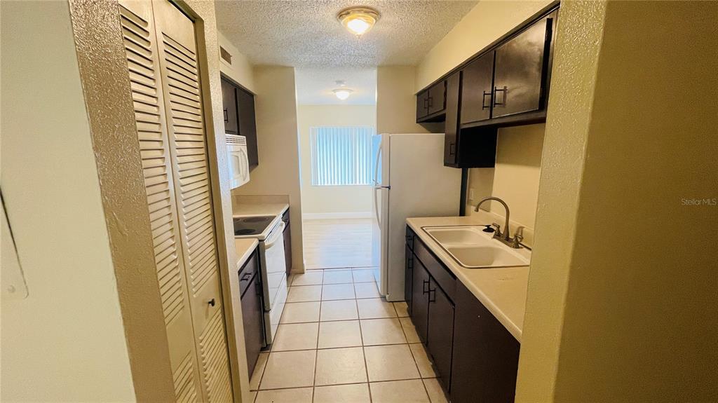A galley kitchen features dark cabinets, white appliances, and light-colored tile flooring — 7504 NEEDLE LEAF PLACE UNIT 68, TAMPA, FL