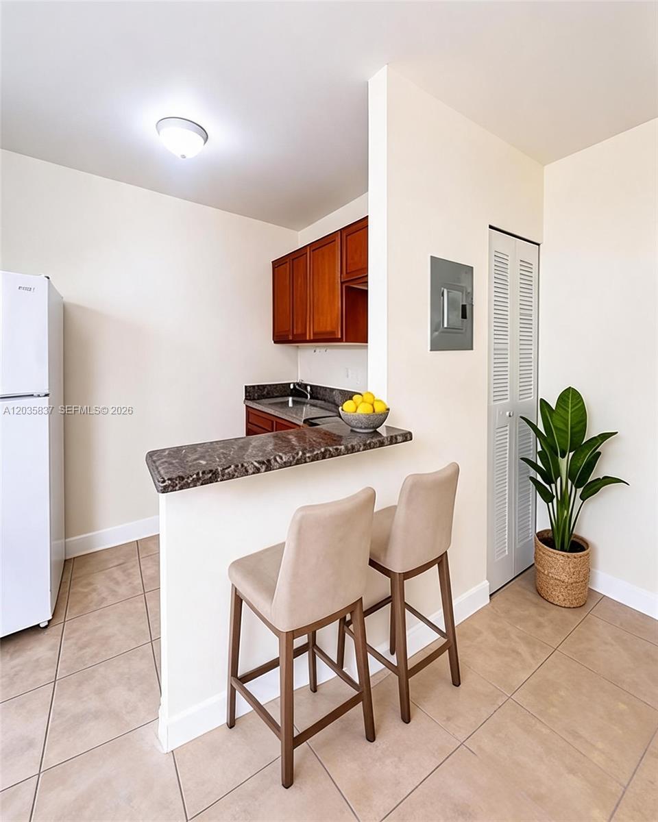 A small kitchen features a breakfast bar with two stools, wood cabinets, and tile flooring — 1533 NW 2nd Ave # 6, Miami FL 33136, MIAMI, FL