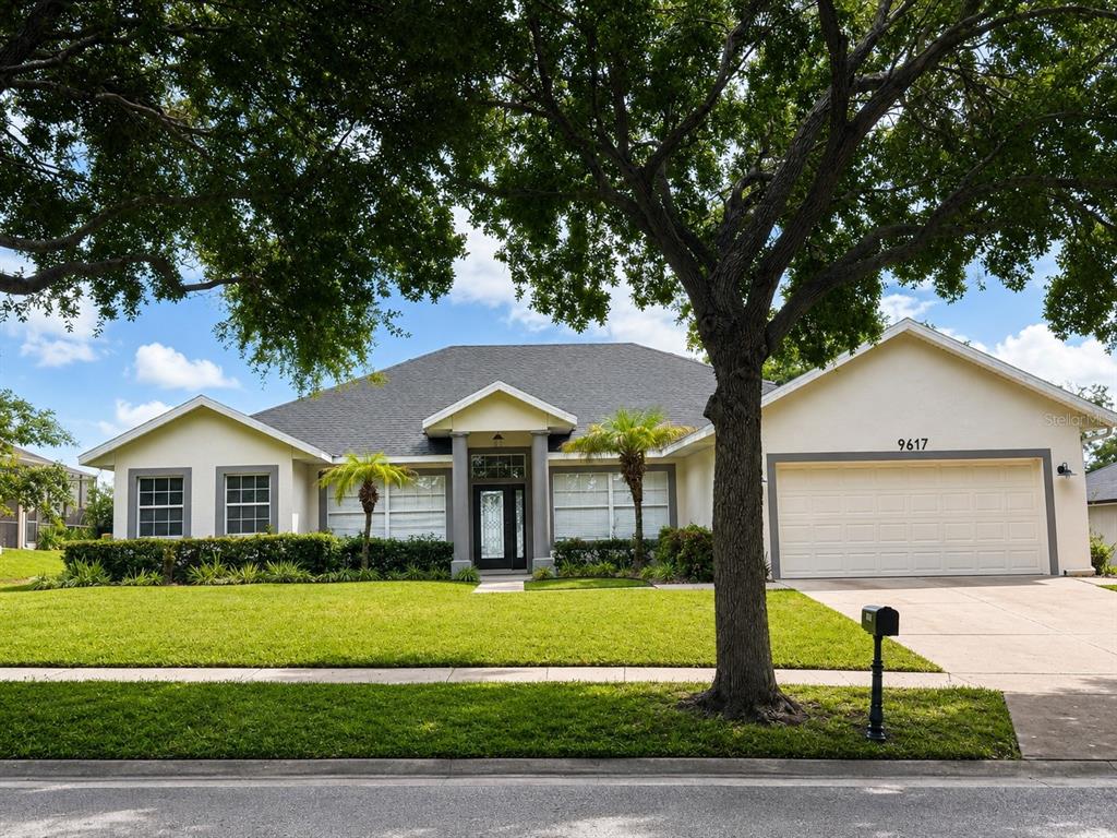 A single-story suburban house with a two-car garage, a front lawn, and a large tree — 9617 SPRING LAKE DRIVE, CLERMONT, FL