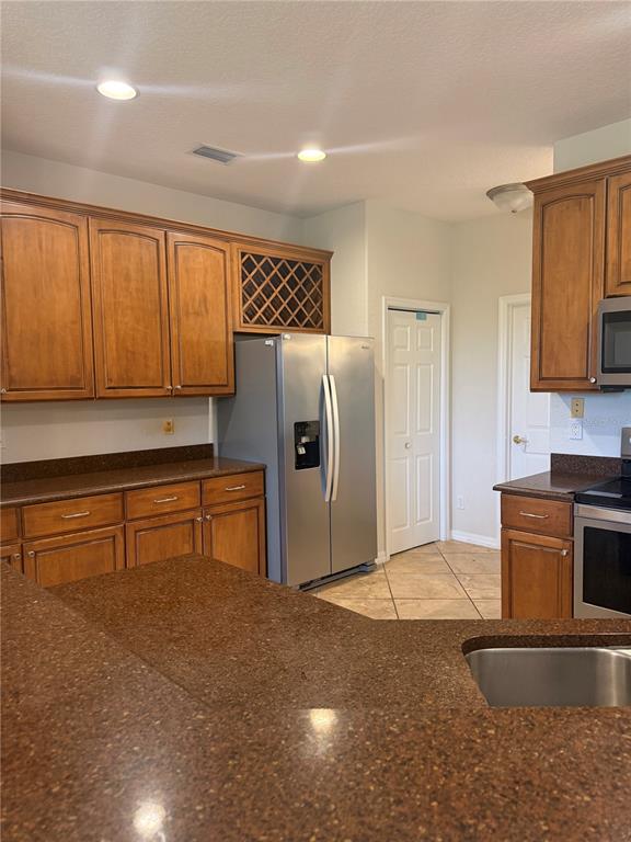 A kitchen features wood cabinets, dark countertops, stainless steel appliances, and tile flooring — 9617 SPRING LAKE DRIVE, CLERMONT, FL
