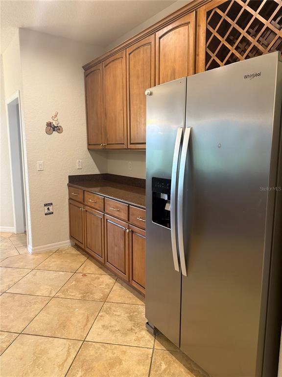 A kitchen features wood cabinets, a stainless steel refrigerator, and tiled flooring — 9617 SPRING LAKE DRIVE, CLERMONT, FL