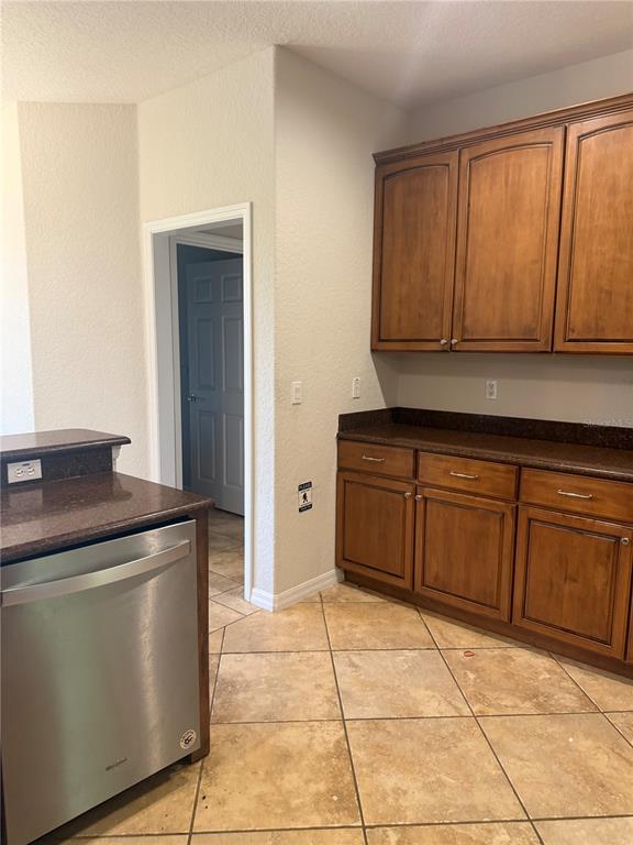 A kitchen features wood cabinets, dark countertops, a stainless steel dishwasher, and tiled flooring — 9617 SPRING LAKE DRIVE, CLERMONT, FL
