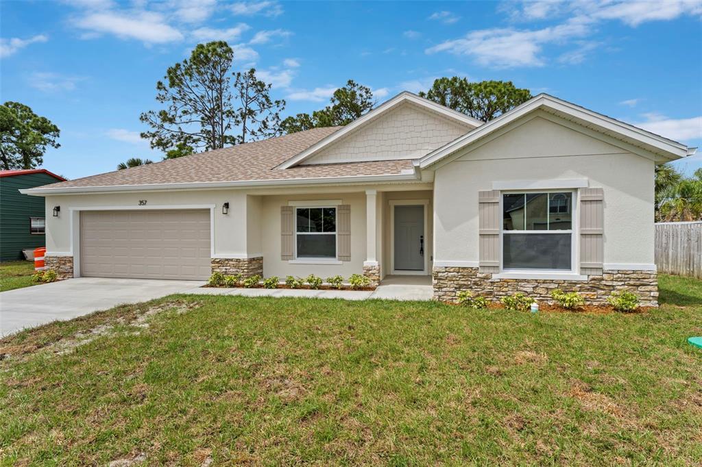 A single-story house with a beige stucco exterior, stone accents, and a two-car garage — 357 GALICIA STREET SW, PALM BAY, FL