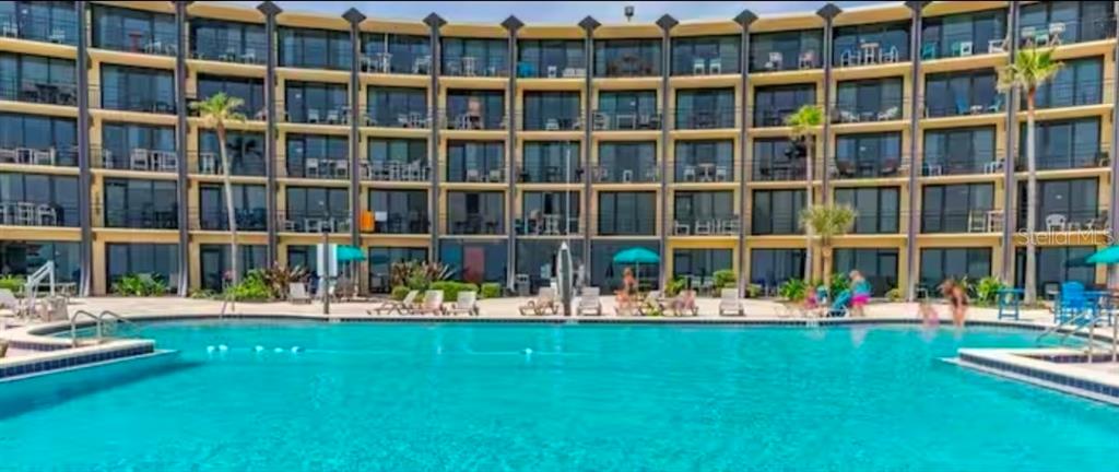 A large swimming pool sits in front of a multi-story, curved residential building — 2301 S ATLANTIC AVENUE UNIT 337, DAYTONA BEACH, FL