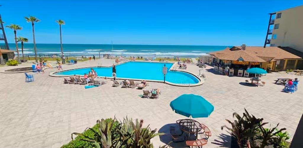 An outdoor swimming pool sits on a paved patio beside a beachside bar and ocean — 2301 S ATLANTIC AVENUE UNIT 337, DAYTONA BEACH, FL
