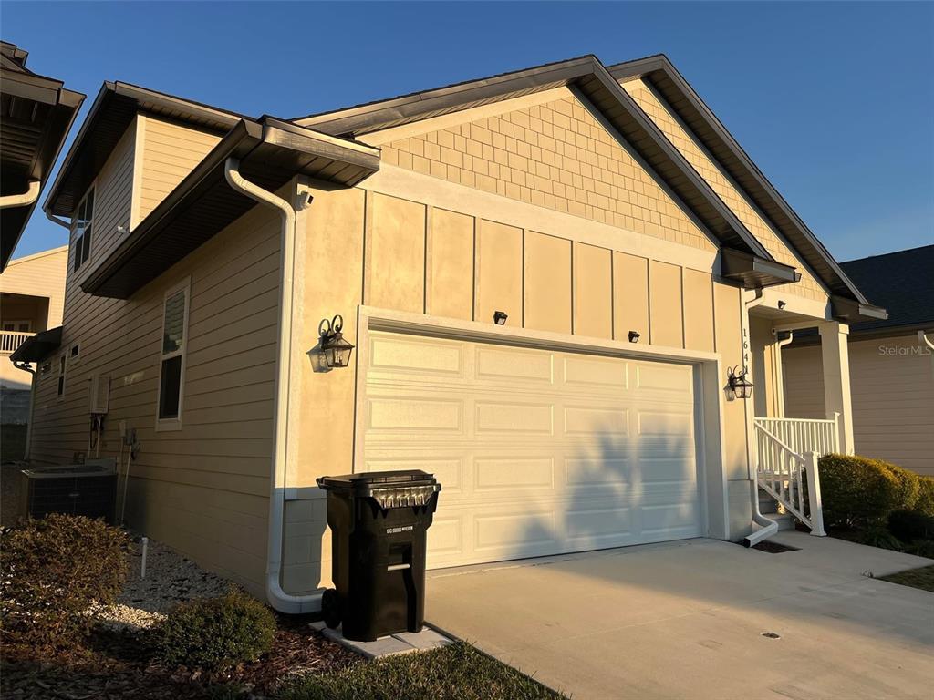 A beige house exterior features a two-car garage, a white railing, and a trash bin — 1641 NW 121ST WAY, GAINESVILLE, FL