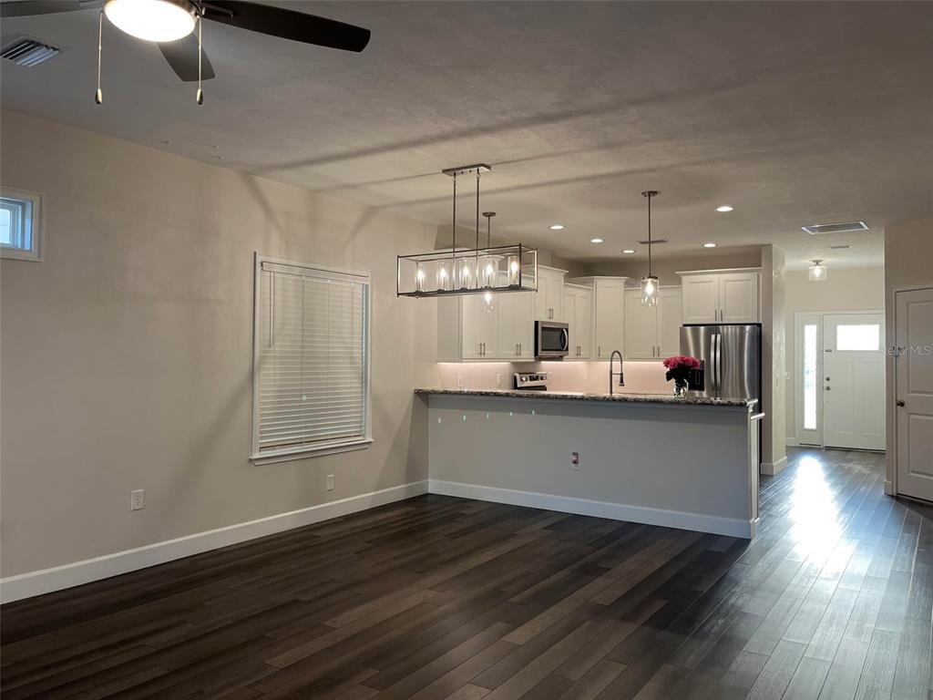 An open-concept kitchen and dining area features dark wood flooring, white cabinetry, and pendant lighting — 1641 NW 121ST WAY, GAINESVILLE, FL