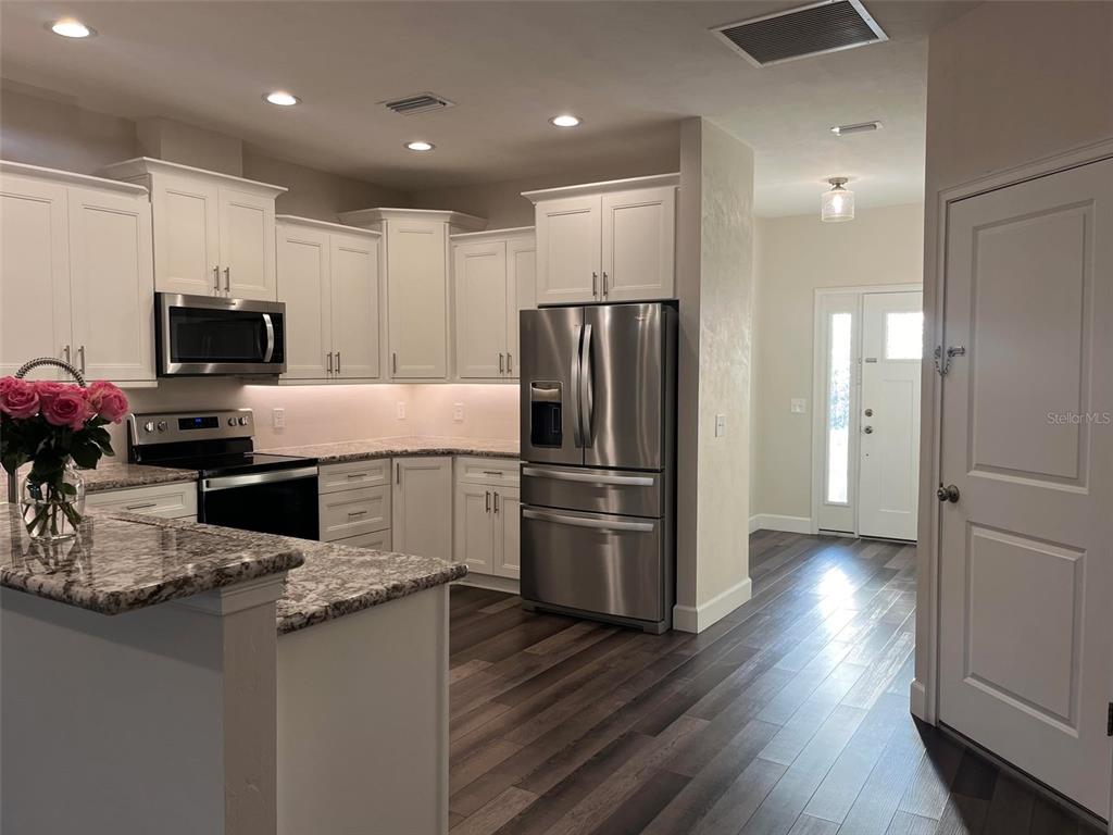 A kitchen with white cabinets, stainless steel appliances, and granite countertops features dark wood flooring — 1641 NW 121ST WAY, GAINESVILLE, FL