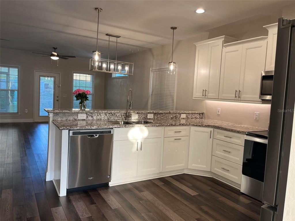 A kitchen features white cabinets, granite countertops, stainless steel appliances, and dark wood-look flooring — 1641 NW 121ST WAY, GAINESVILLE, FL
