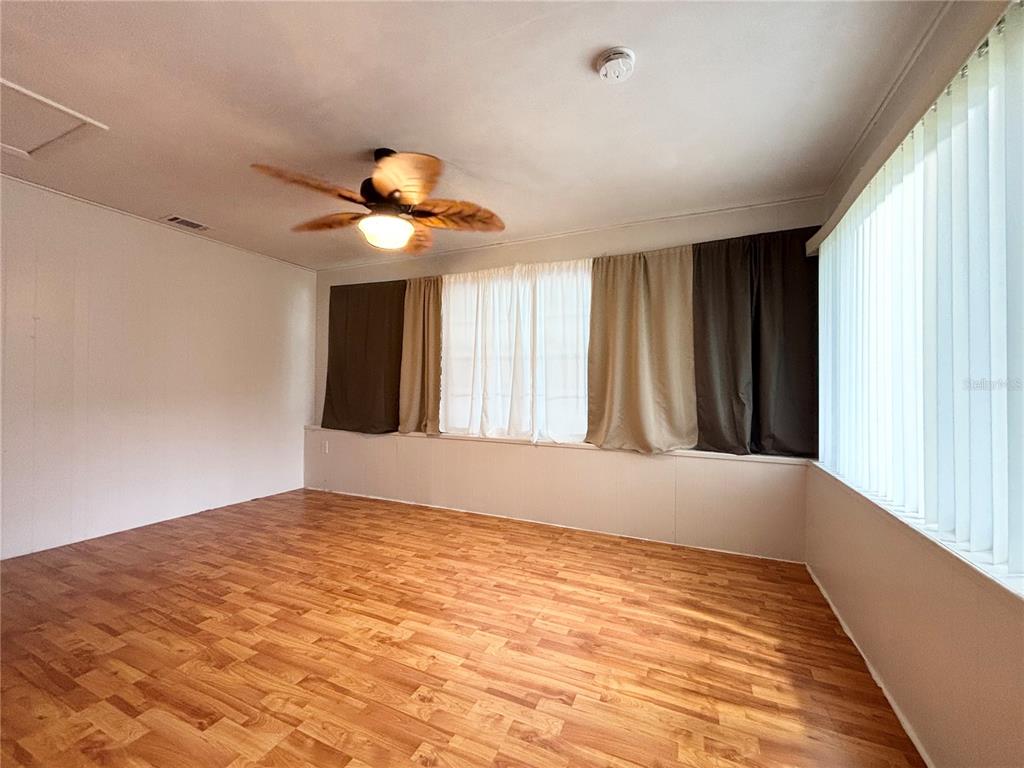 An empty room features wood-look flooring, a ceiling fan, and large windows with curtains — 26 S OSCEOLA STREET, BEVERLY HILLS, FL