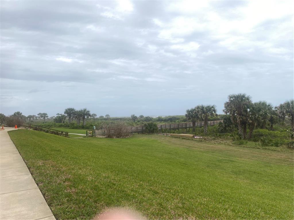 A grassy lawn leads to a wooden fence and palm trees under a cloudy sky — 60 SURFVIEW DRIVE UNIT 121, PALM COAST, FL