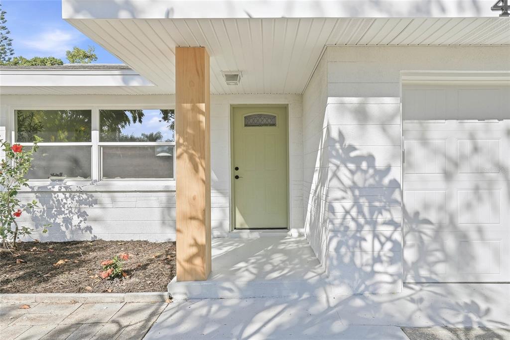 A light green front door sits under a covered porch with a natural wood post — 4720 MOHEGAN ROAD, ST PETERSBURG, FL