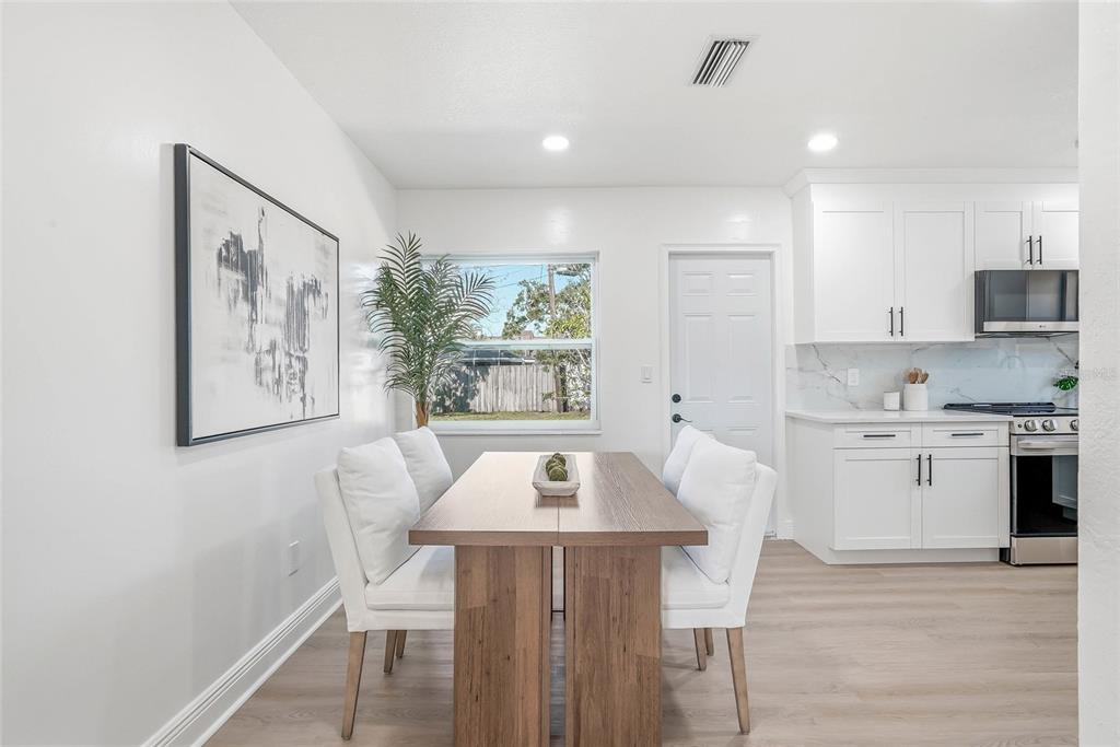 A dining area with a wooden table and white chairs sits adjacent to a white kitchen — 4720 MOHEGAN ROAD, ST PETERSBURG, FL