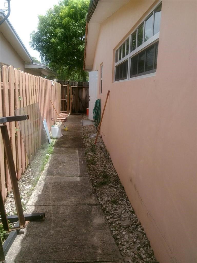 A narrow concrete walkway runs alongside a peach-colored house exterior with a wooden fence — 6764 AZALEA Drive, Miramar FL 33023, MIRAMAR, FL