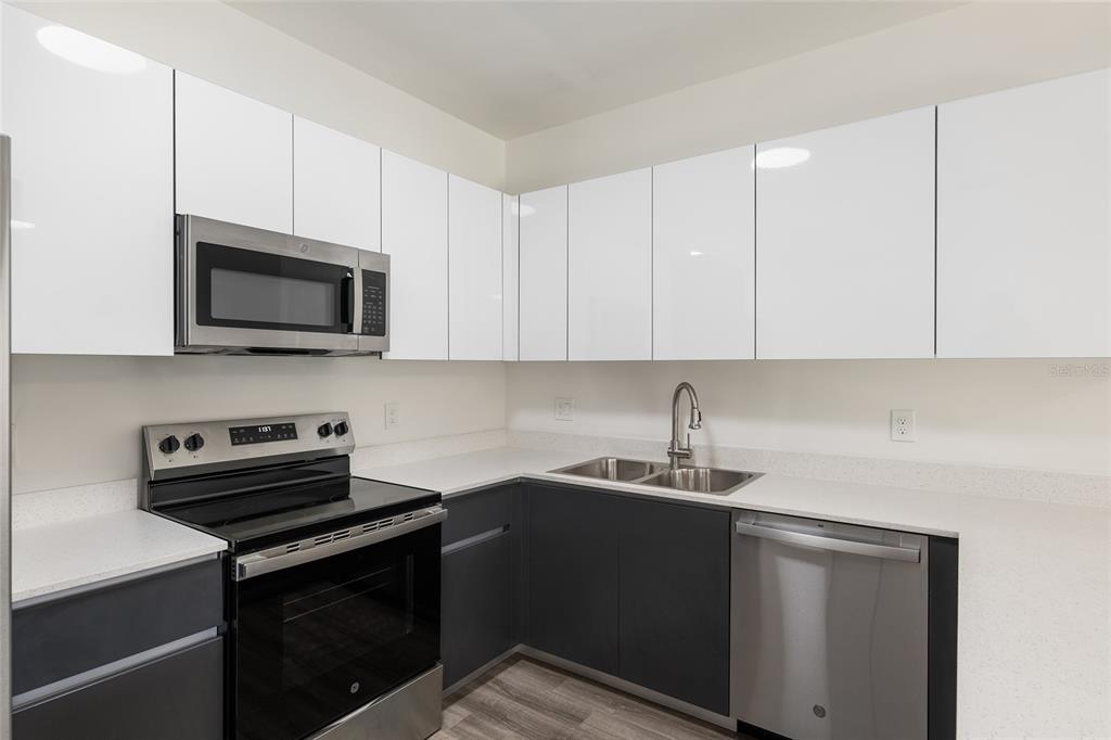 A modern kitchen features white upper cabinets, dark lower cabinets, and stainless steel appliances — 1581 NW 29TH ROAD UNIT 2, GAINESVILLE, FL