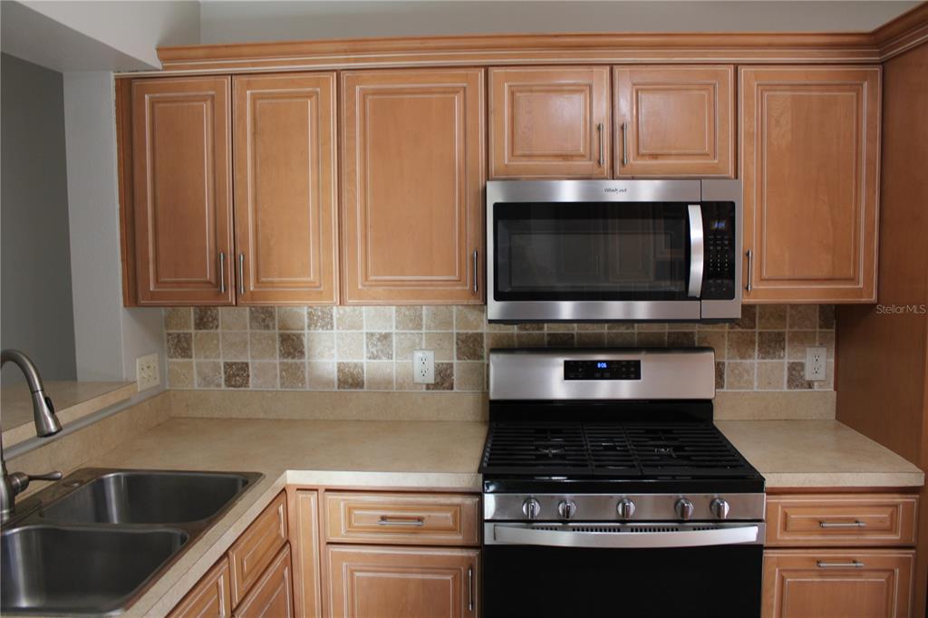 A kitchen features light wood cabinets, stainless steel appliances, and a tiled backsplash — 3931 DAY BRIDGE PLACE, ELLENTON, FL