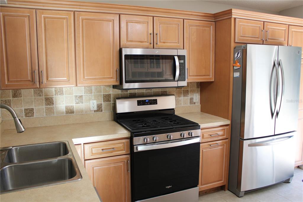 A kitchen features light wood cabinets, stainless steel appliances, and a tiled backsplash — 3931 DAY BRIDGE PLACE, ELLENTON, FL