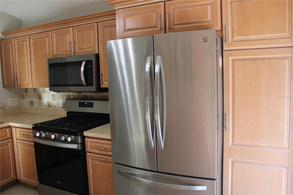 A kitchen features stainless steel appliances, light wood cabinets, and a tiled backsplash — 3931 DAY BRIDGE PLACE, ELLENTON, FL