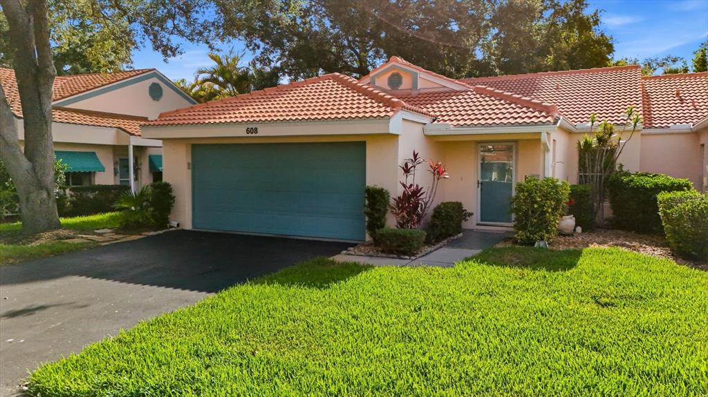 A single-story house with a teal garage door, orange tile roof, and a front lawn — 608 TYSON TERRACE UNIT 8, VENICE, FL