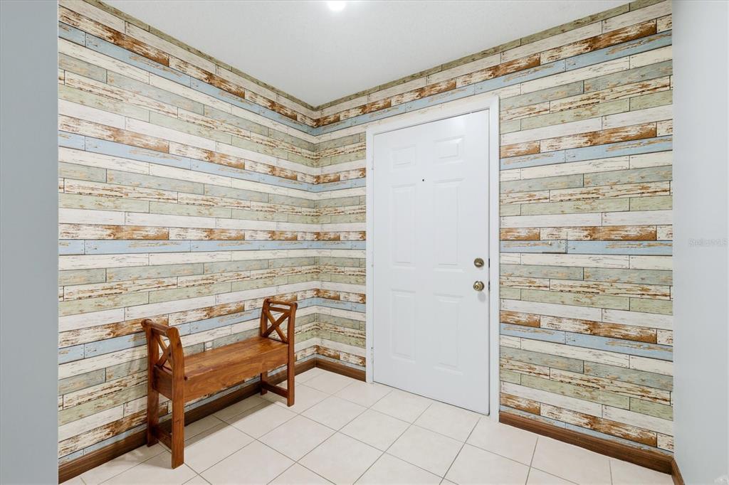 An entryway features white tiled floors, a wooden bench, and walls with rustic wood-look wallpaper — 608 TYSON TERRACE UNIT 8, VENICE, FL