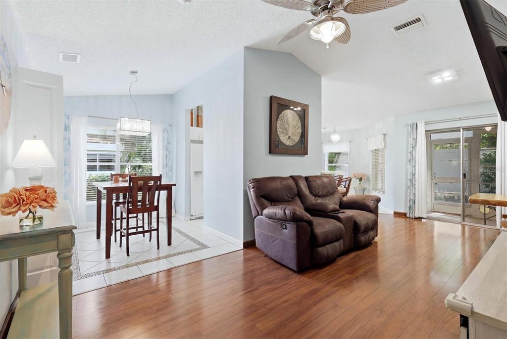 A living room with hardwood floors and a brown loveseat adjacent to a tiled dining area — 608 TYSON TERRACE UNIT 8, VENICE, FL