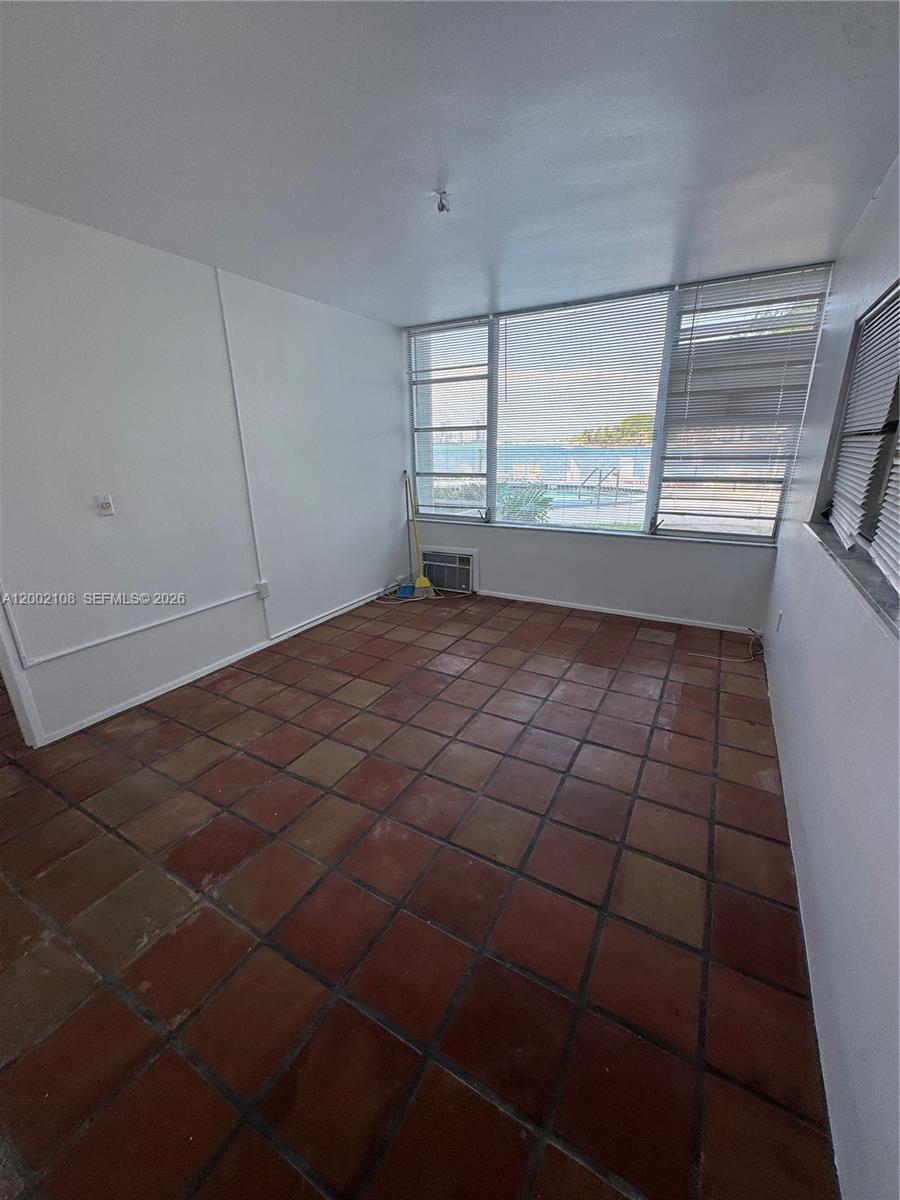 An empty room features terracotta tile flooring, white walls, and large windows overlooking a pool — 10281 E Bay Harbor Dr # C2, Bay Harbor Islands FL 33154, BAY HARBOR ISLANDS, FL