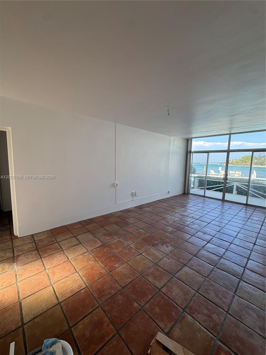 An empty room features terracotta tile flooring, white walls, and large windows overlooking the water — 10281 E Bay Harbor Dr # C2, Bay Harbor Islands FL 33154, BAY HARBOR ISLANDS, FL