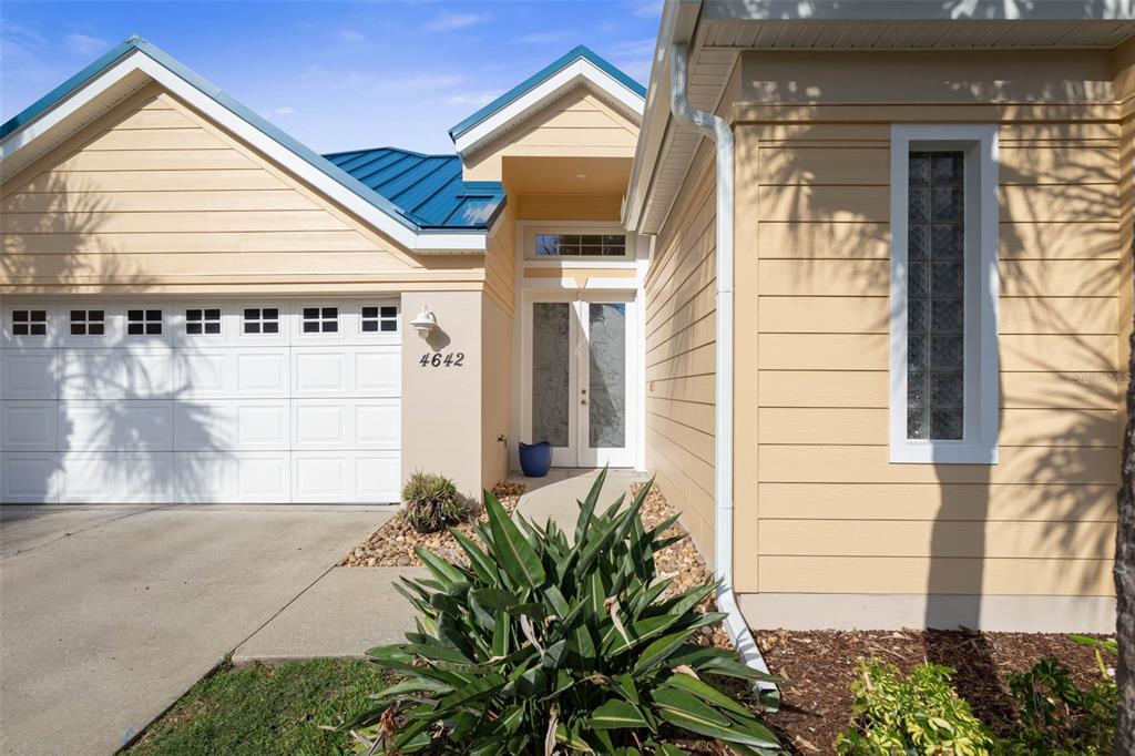 The exterior of a tan house features a white garage door, double front doors, and landscaping — 4642 RIVERWALK VILLAGE COURT, PONCE INLET, FL
