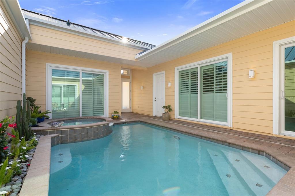 A swimming pool and hot tub are situated in a courtyard between yellow-sided house walls — 4642 RIVERWALK VILLAGE COURT, PONCE INLET, FL
