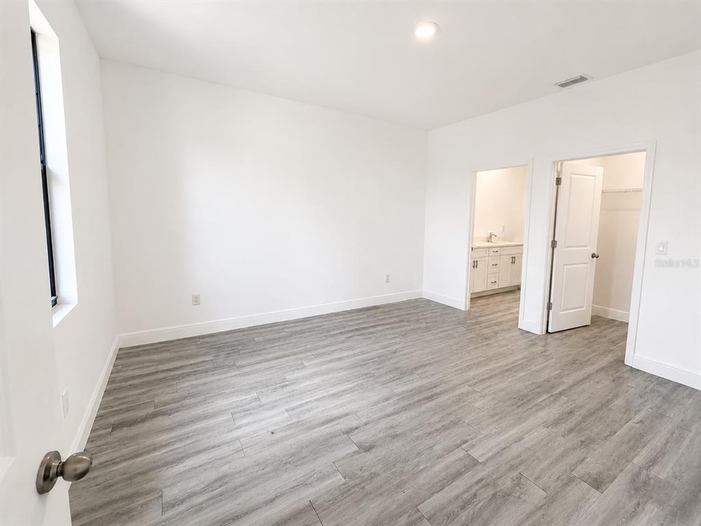 A bedroom with light gray wood-look flooring, white walls, a bathroom doorway, and a closet — 6203 FOREST COURT, LABELLE, FL