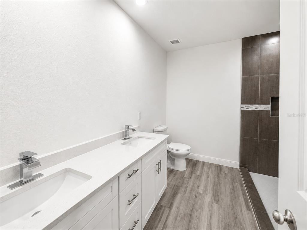 A modern bathroom features a double vanity with white cabinets, a toilet, and a tiled shower — 6203 FOREST COURT, LABELLE, FL