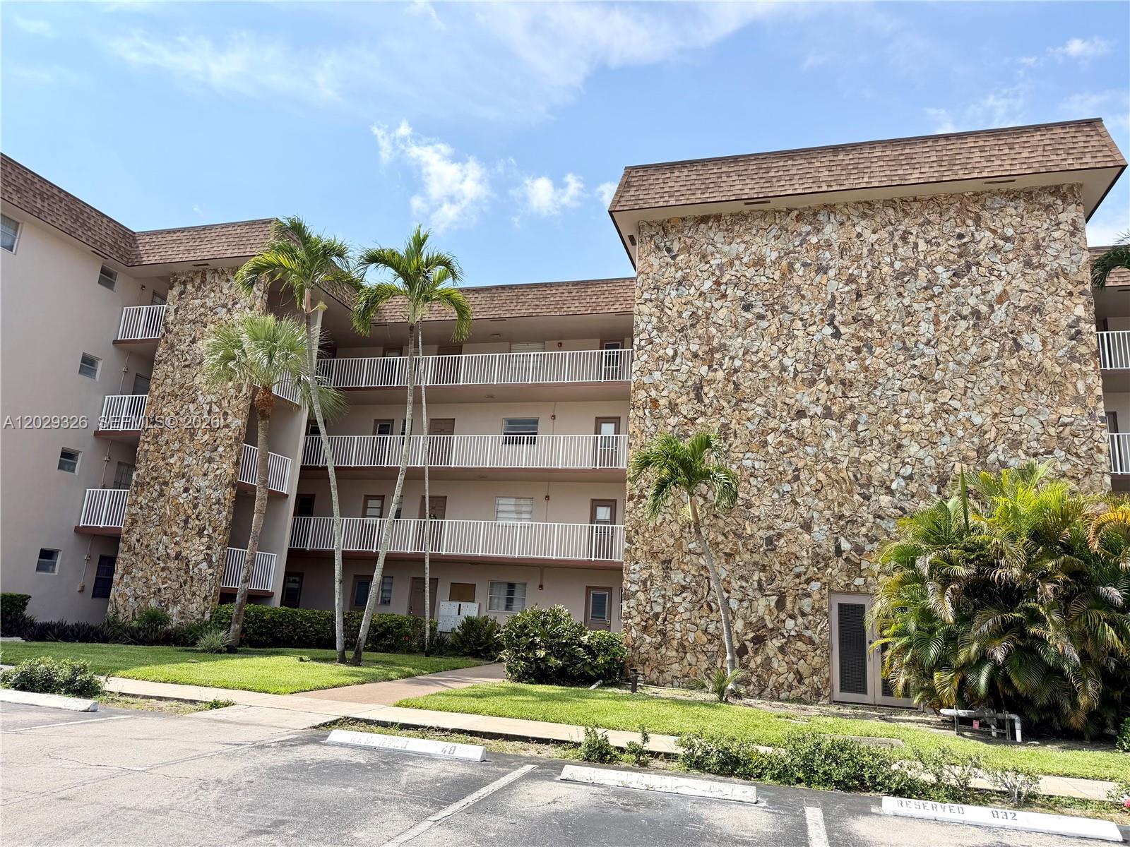 A multi-story apartment building features stone-clad exterior walls, white balconies, and surrounding palm trees — 8101 SW 24th Ct # 405, Davie FL 33324, DAVIE, FL