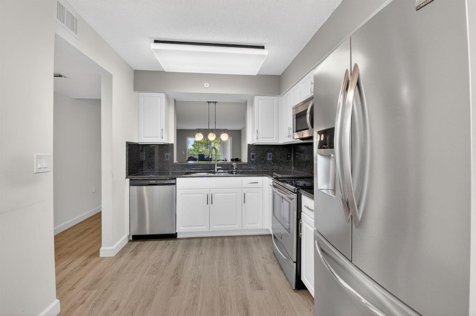 A kitchen with white cabinets, stainless steel appliances, and dark countertops features a pass-through window — 6080 Huntwick Terrace # 405, Delray Beach FL 33484, DELRAY BEACH, FL