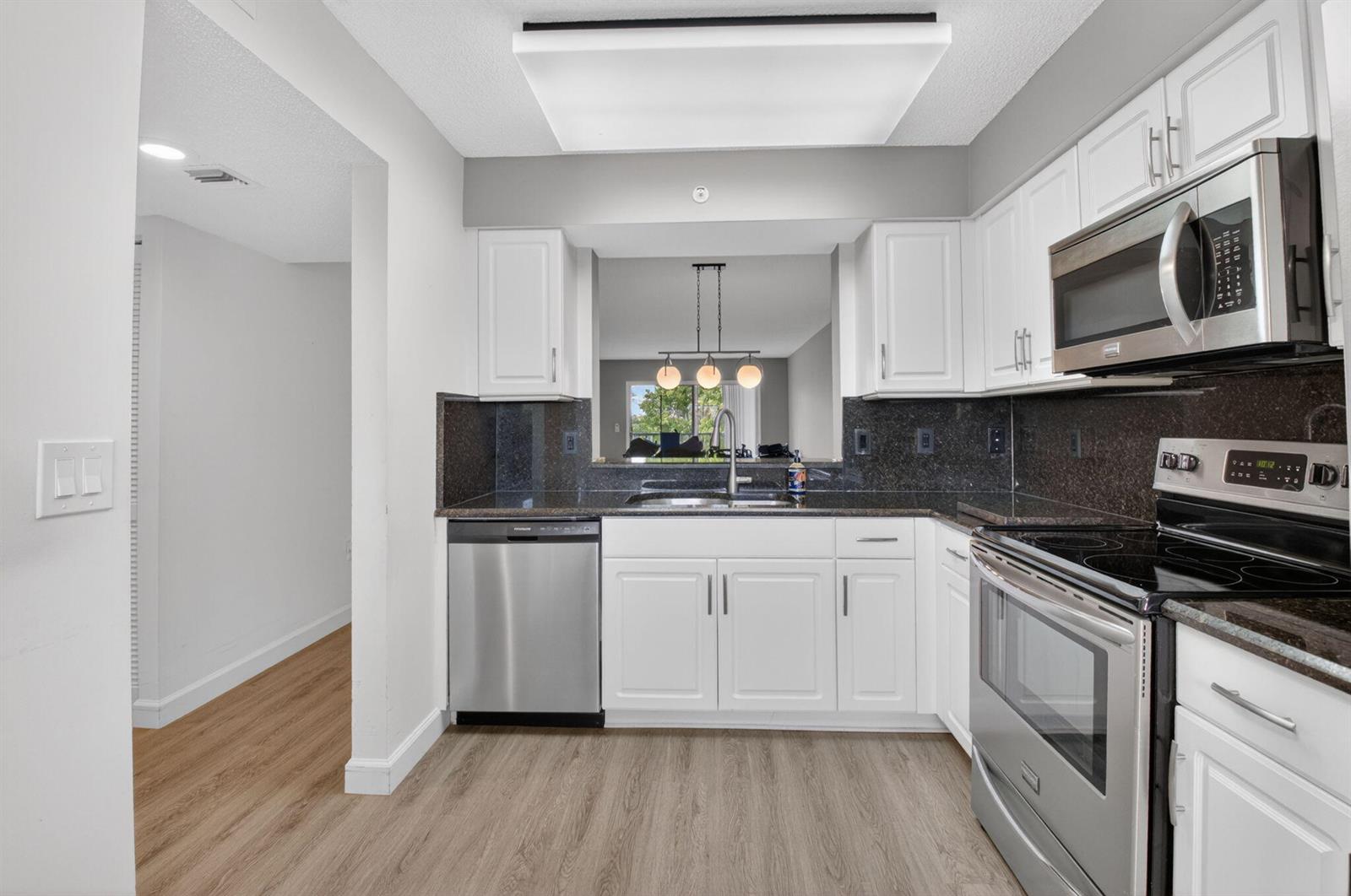 A kitchen with white cabinets, dark granite countertops, stainless steel appliances, and light wood flooring — 6080 Huntwick Terrace # 405, Delray Beach FL 33484, DELRAY BEACH, FL