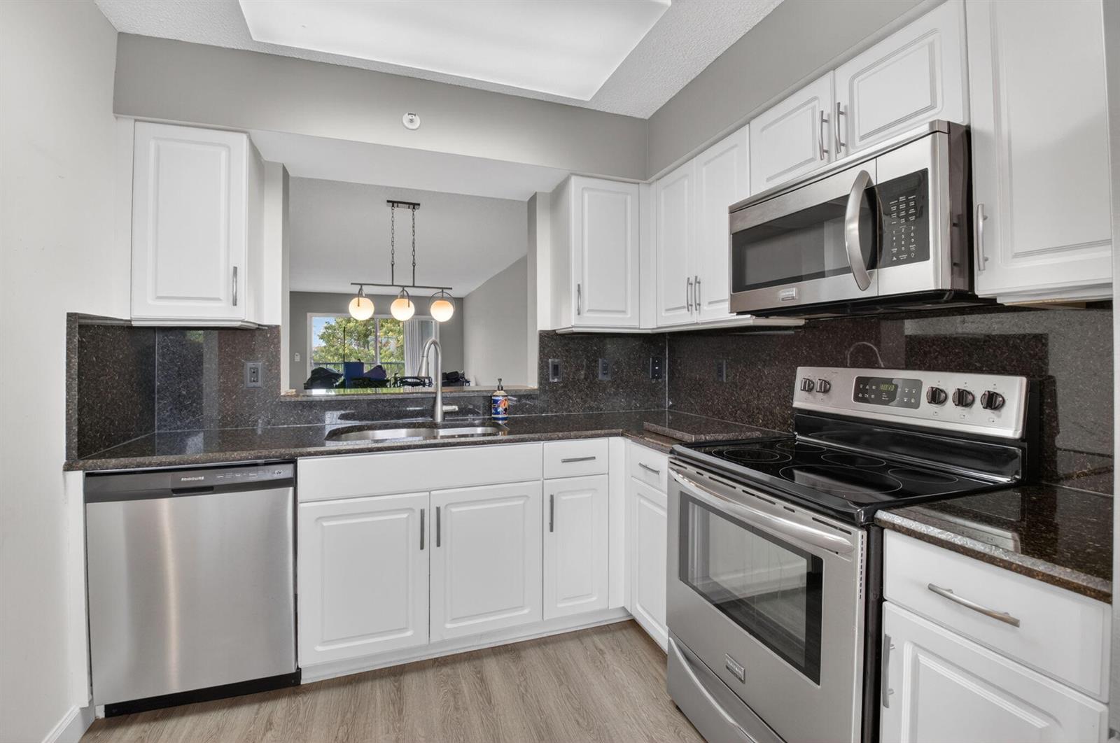 A kitchen with white cabinets, dark granite countertops, and stainless steel appliances — 6080 Huntwick Terrace # 405, Delray Beach FL 33484, DELRAY BEACH, FL