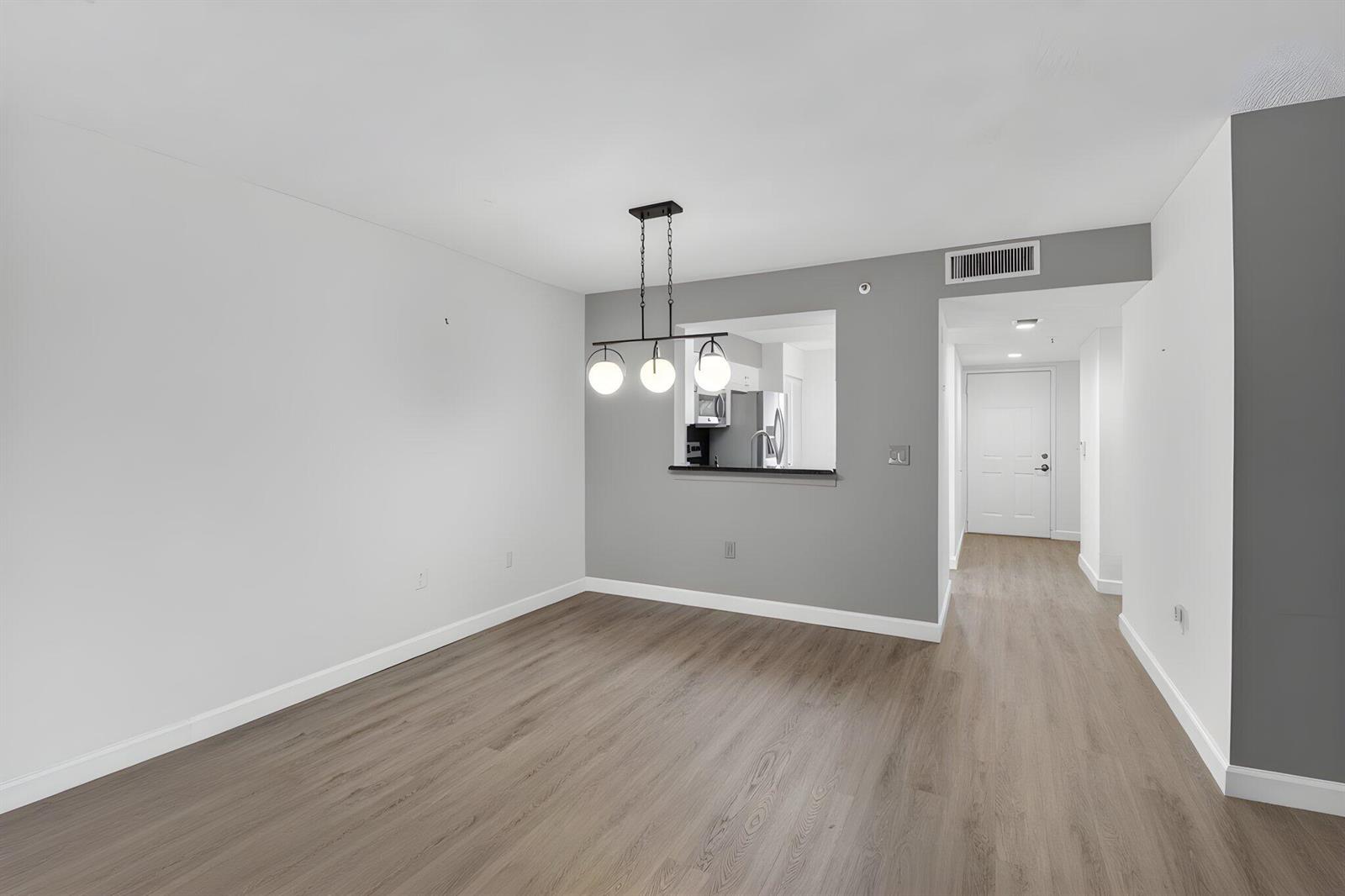 An empty dining area features light wood-look flooring, white walls, and a modern pendant light — 6080 Huntwick Terrace # 405, Delray Beach FL 33484, DELRAY BEACH, FL