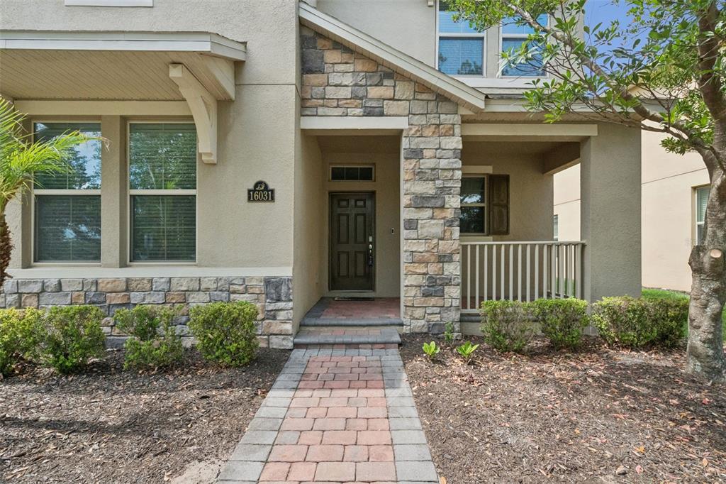A paved walkway leads to the front entrance of a house with stone accents — 16031 PEBBLE BLUFF LOOP, WINTER GARDEN, FL