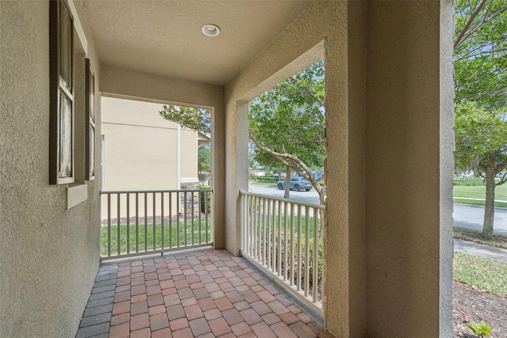 A covered porch features a brick paver floor and white railings overlooking a residential street — 16031 PEBBLE BLUFF LOOP, WINTER GARDEN, FL