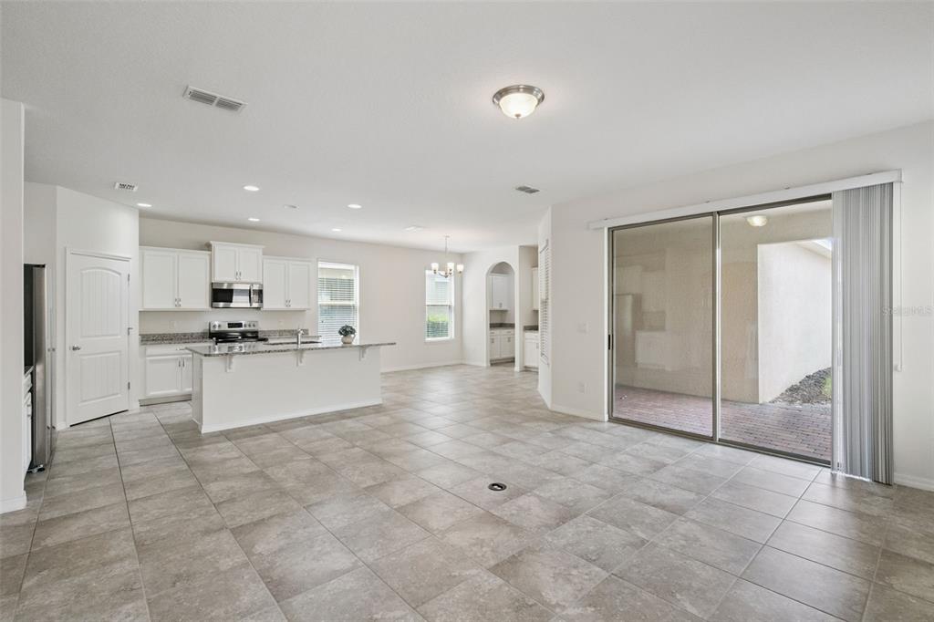 An open-concept kitchen and living area with tile floors, white cabinets, and sliding glass doors — 16031 PEBBLE BLUFF LOOP, WINTER GARDEN, FL