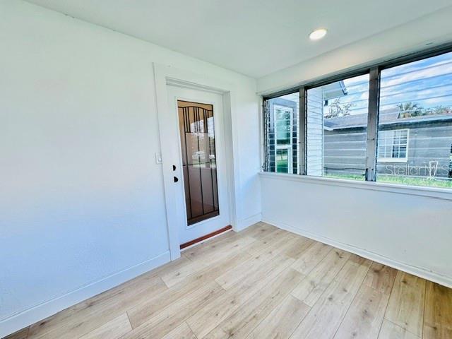 A sunroom with light wood-look flooring, white walls, and a glass-paneled door — 624 ILLINOIS AVENUE, ST CLOUD, FL