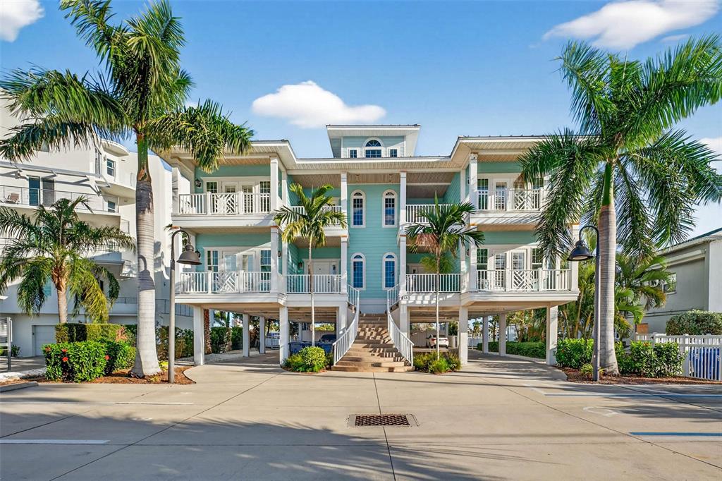 A light blue, multi-story elevated house with white railings and palm trees in the front — 255 104TH AVENUE, TREASURE ISLAND, FL