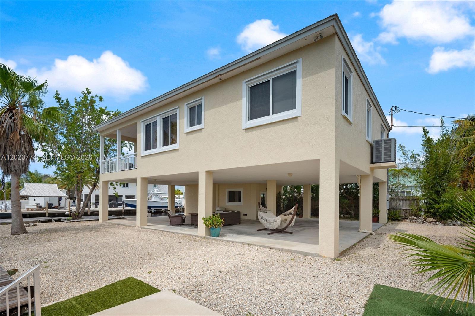 A two-story house on stilts features a covered ground-level patio and a gravel yard — KEY LARGO, FL