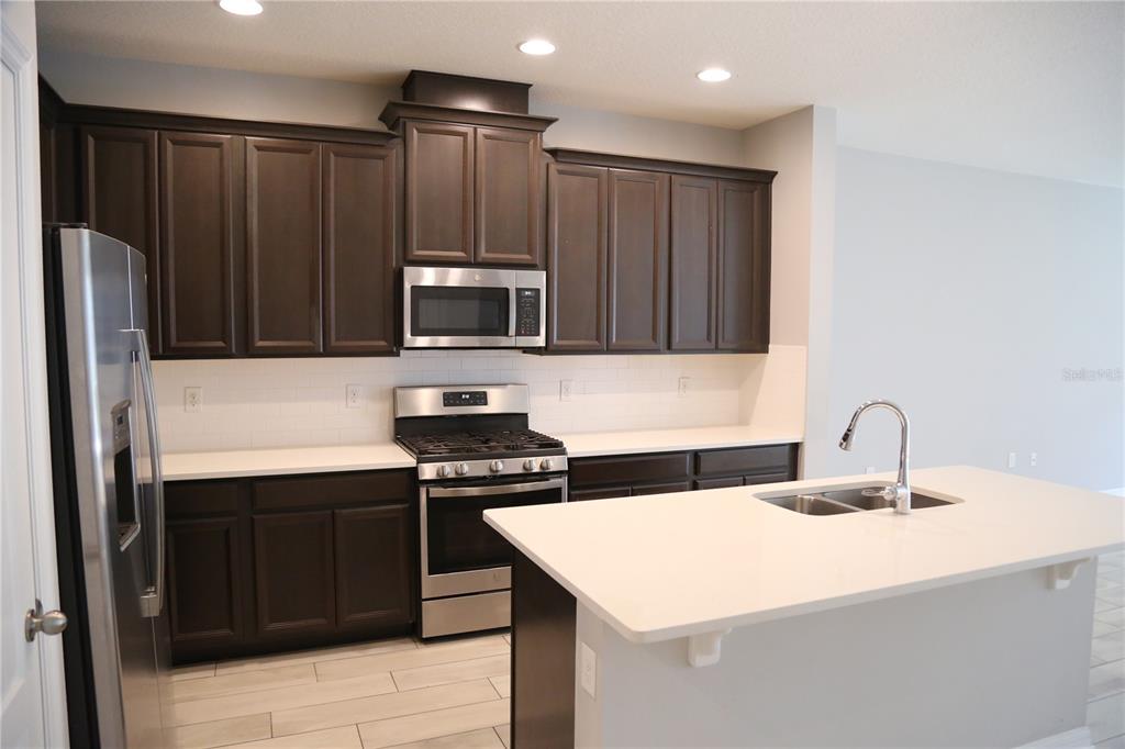 A kitchen features dark wood cabinets, stainless steel appliances, white countertops, and a center island — 229 RUSTIC LOOP, SANFORD, FL