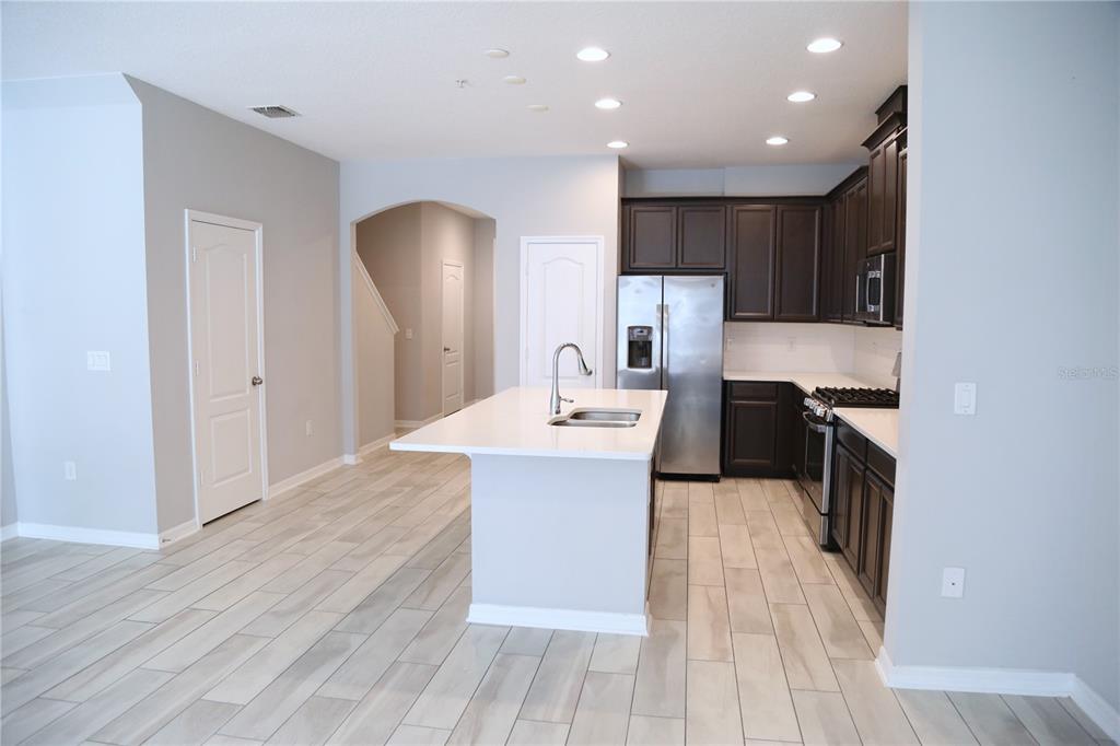 A kitchen with dark cabinets, a white island, stainless steel appliances, and light wood-look flooring — 229 RUSTIC LOOP, SANFORD, FL