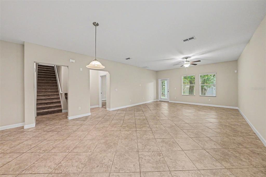 An empty living room features beige walls, large floor tiles, a ceiling fan, and stairs — 11809 TWILIGHT DARNER PLACE, RIVERVIEW, FL