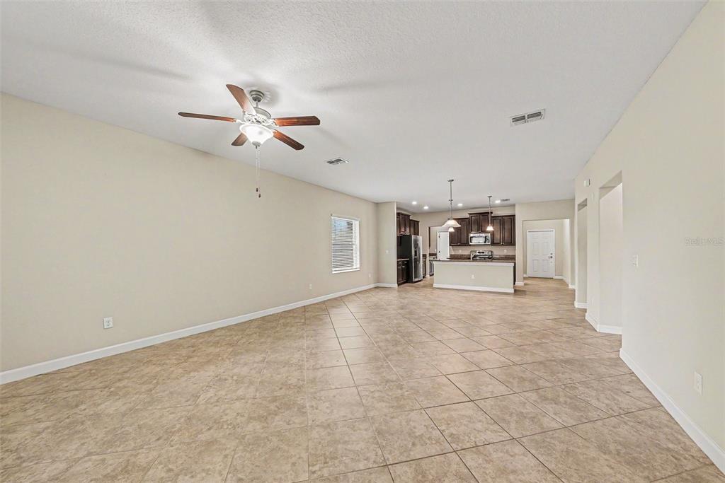 An open-concept living area features beige walls, tile flooring, and a kitchen in the back — 11809 TWILIGHT DARNER PLACE, RIVERVIEW, FL