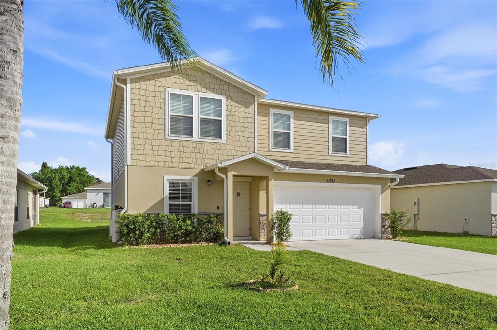 A two-story house with tan siding, a white garage door, and a small front porch — 1637 MARBLE STREET, SEBRING, FL
