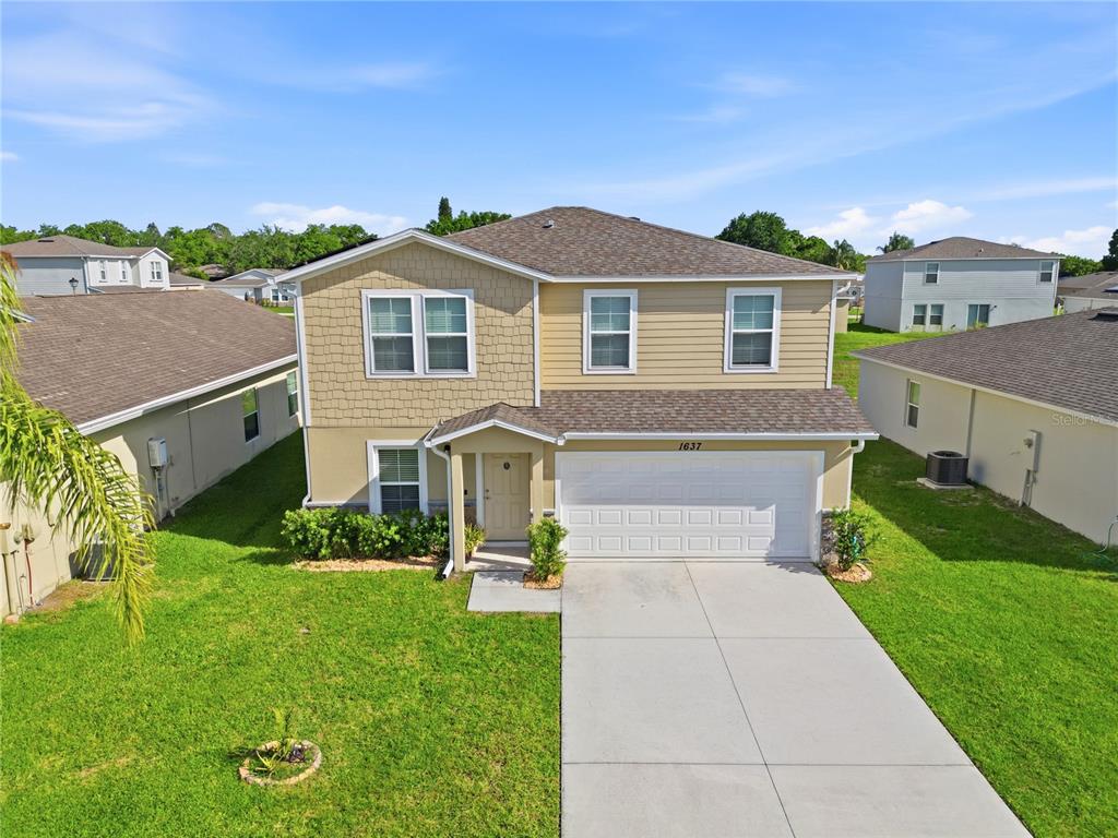 A two-story suburban house with tan siding, a shingled roof, and a two-car garage — 1637 MARBLE STREET, SEBRING, FL