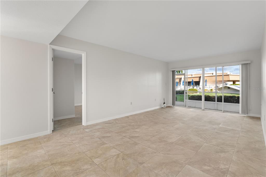 A bright living room features light-colored tile flooring, white walls, and a sliding glass door — 1080 BAL HARBOR BOULEVARD UNIT 11B, PUNTA GORDA, FL